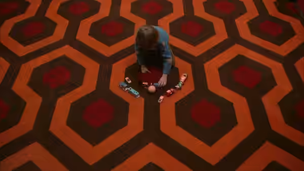 Danny (Danny Lloyd) sits on a geometric carpet playing with toy trucks and blocks