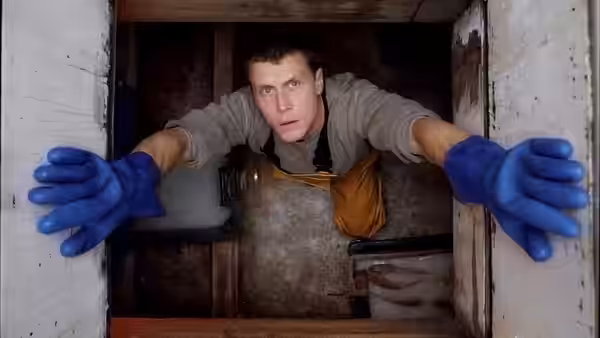 A man in blue gloves and overalls climbs out through an open hatch