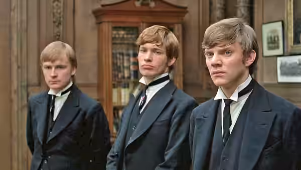 three young men in dark suits standing formally in a wood-panelled hall