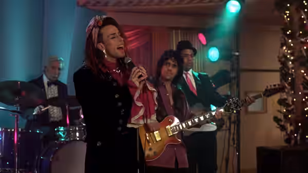 George (Alexis Arquette) singing into a microphone on stage with the band