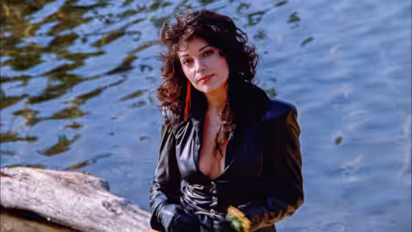 Apollonia (Apollonia Kotero) stands beside the water, holding a small bouquet