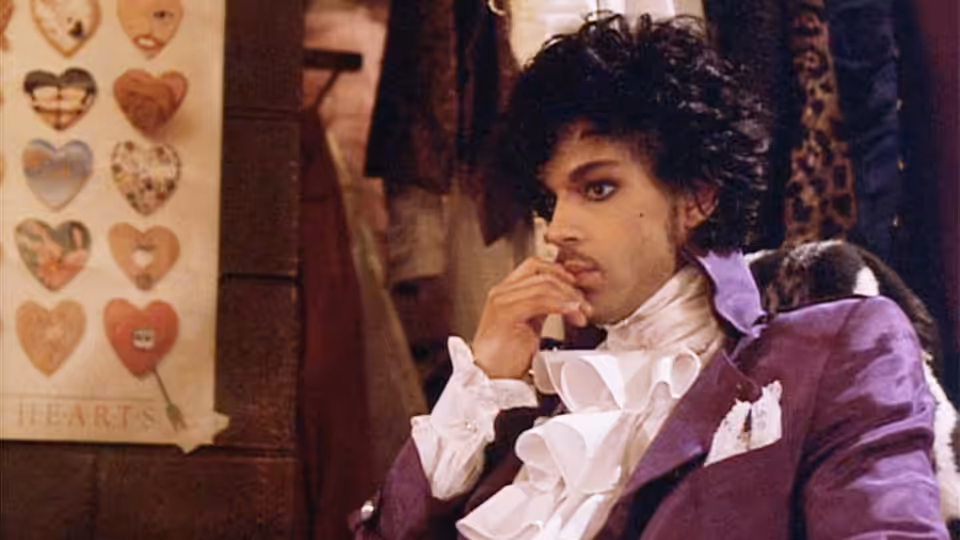The Kid (Prince) sits pensively in a shop surrounded by clothing and heart displays