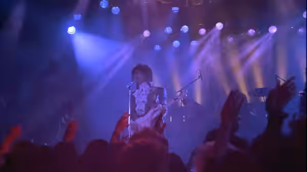 The Kid (Prince) plays guitar onstage as fans raise their hands beneath concert lights