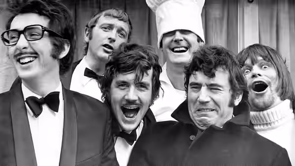 Six men in suits and chef hat pose with mouths wide open