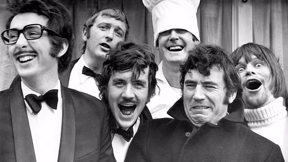 Six men in suits and chef hat pose with mouths wide open