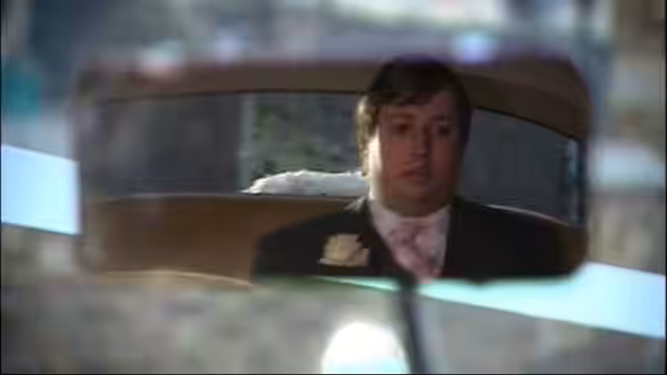 Mark Corrigan (David Mitchell) wearing a tuxedo seen in a rearview mirror