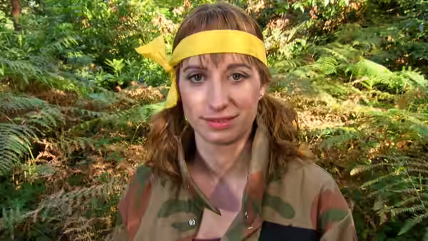 a woman in camouflage and yellow headband standing in a forest
