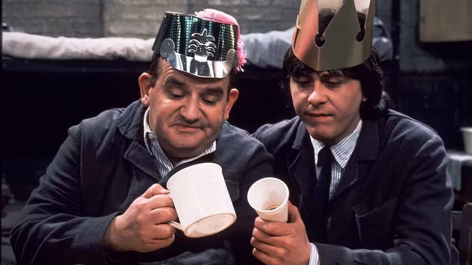 Fletcher (Ronnie Barker) and Godber (Richard Beckinsale) wearing party hats while holding mugs