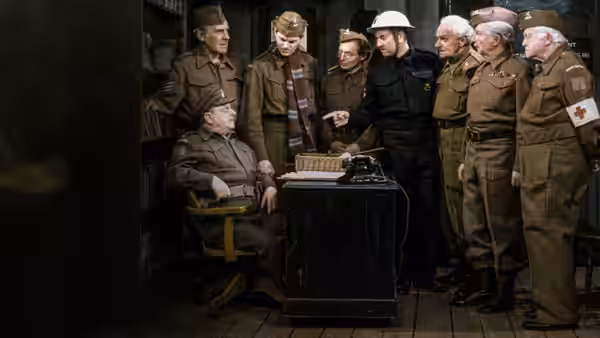Captain Mainwaring seated at a desk with typewriter as soldiers gather around