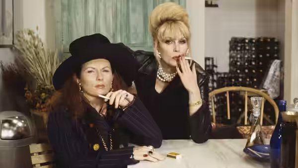 Patsy (Joanna Lumley) and Edina (Jennifer Saunders) seated at a table smoking cigarettes