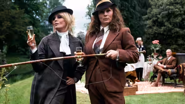 Edina (Jennifer Saunders) and Patsy (Joanna Lumley) holding champagne glasses and a long pole outdoors
