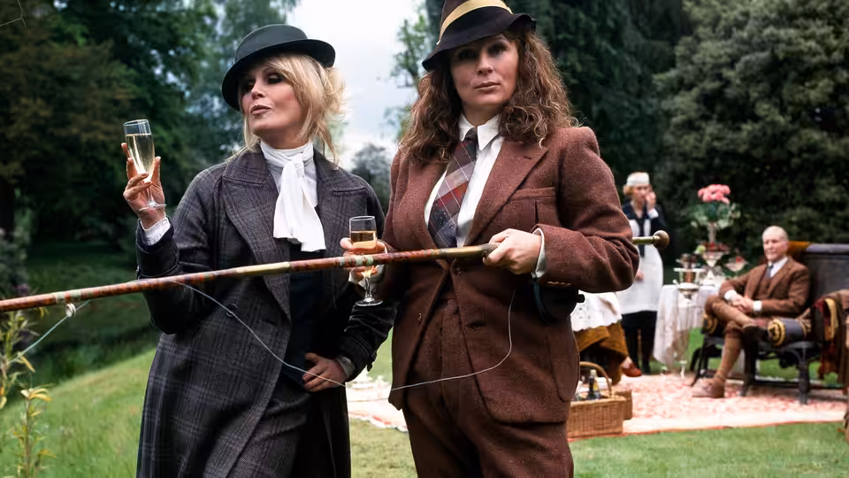 Edina (Jennifer Saunders) and Patsy (Joanna Lumley) holding champagne glasses and a long pole outdoors