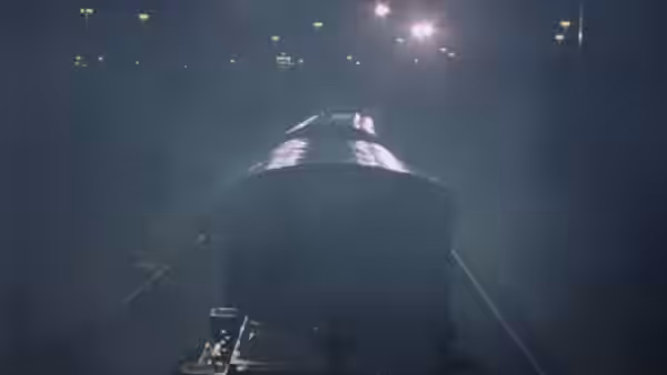 A train moves through a dark foggy railway station at night