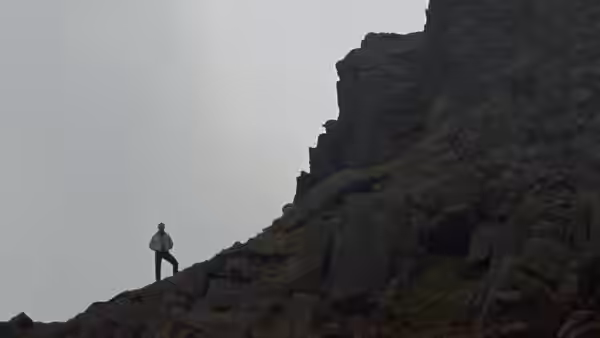A man stands on a rocky hillside under a grey sky