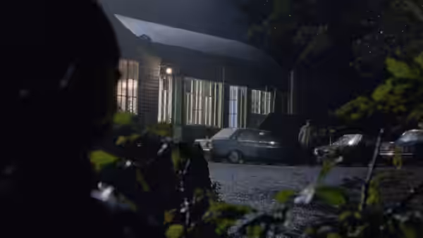 A man stands by parked cars outside a building at night