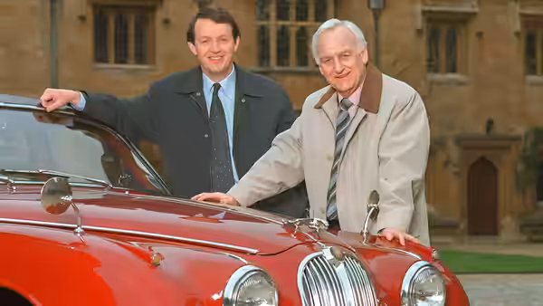Detective Sergeant Lewis (Kevin Whately) and Chief Inspector Morse (John Thaw) stand by a red car