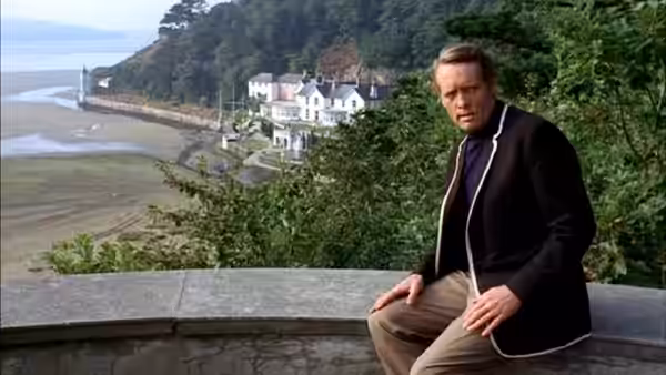 Number Six (Patrick McGoohan) seated on a wall overlooking the Village