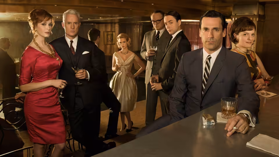 Don Draper (Jon Hamm) and Joan Holloway (Christina Hendricks) stand at a bar with other office workers