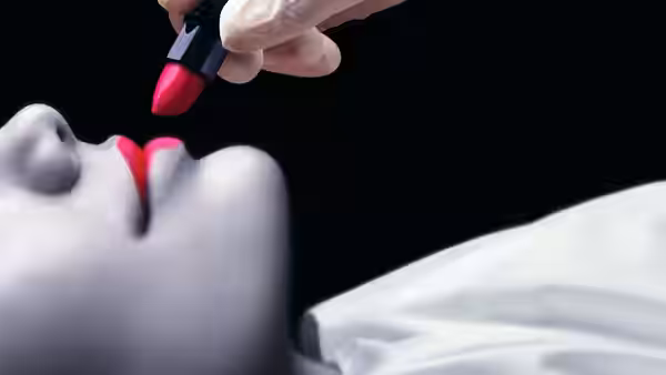 a gloved hand applying red lipstick to a reclining face