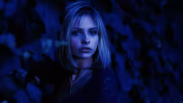 Buffy Summers (Sarah Michelle Gellar) standing in a dark blue leafy setting