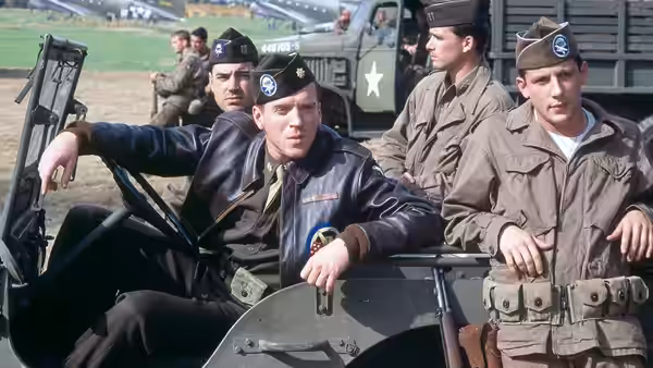 An officer seated in a jeep speaking with soldiers at camp