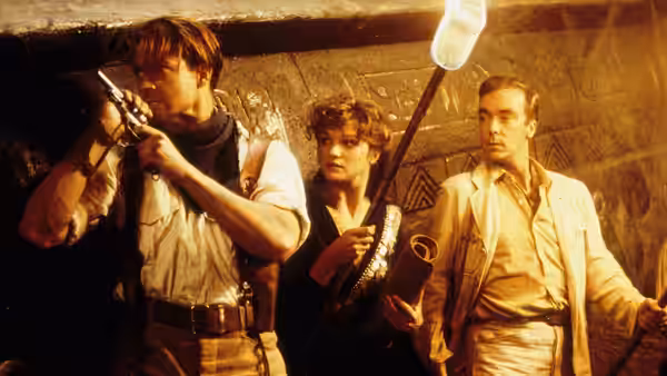 Rick O'Connell (Brendan Fraser) aims a pistol as Evelyn Carnahan (Rachel Weisz) and Jonathan Carnahan (John Hannah) watch in a tomb