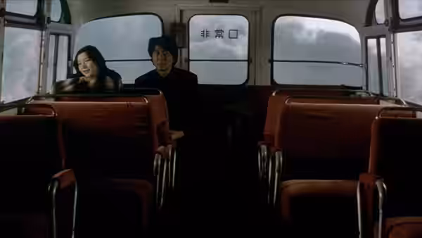 A man and woman sit together in the rear of an almost empty bus