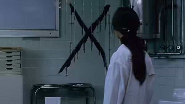 A woman in a white coat examines a large painted X on a tiled wall