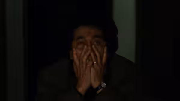 A distressed man covers his mouth with both hands in a dark room