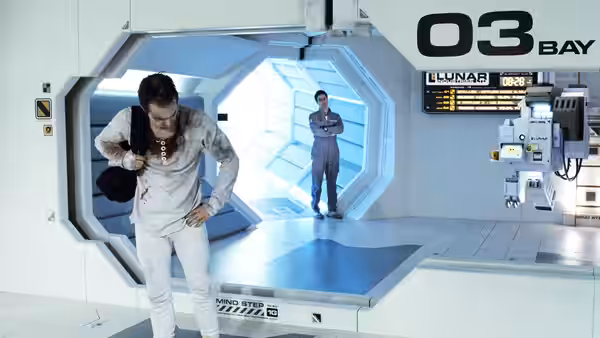 A man in a white spacesuit facing another in a lunar bay
