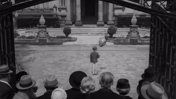 A lone man crosses a courtyard as formally dressed guests watch