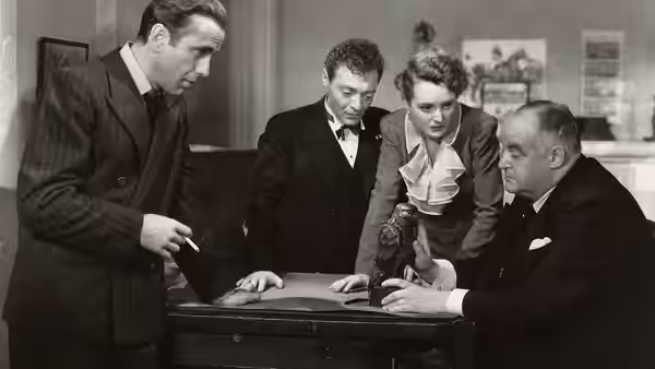 Samuel Spade (Humphrey Bogart), Joel Cairo (Peter Lorre), Brigid O'Shaughnessy (Mary Astor) and Kasper Gutman (Sydney Greenstreet) examine the Maltese Falcon on a desk