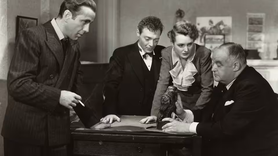 Samuel Spade (Humphrey Bogart), Joel Cairo (Peter Lorre), Brigid O'Shaughnessy (Mary Astor) and Kasper Gutman (Sydney Greenstreet) examine the Maltese Falcon on a desk