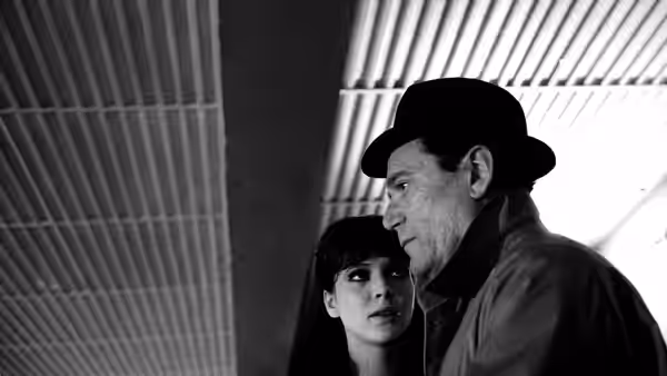 Lemmy Caution (Eddie Constantine) and Natacha von Braun (Anna Karina) stand beneath a striped ceiling