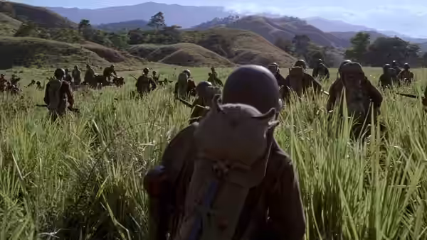 A soldier with backpack walking through a grassy field with troops