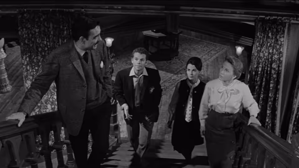 Four visitors climb the staircase inside a dark, ornate mansion