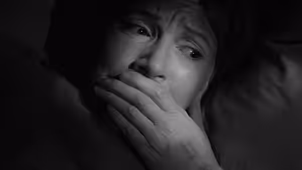 A frightened woman covers her mouth in the darkness