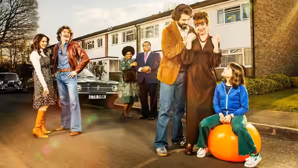 Adults stand on a suburban street while a girl sits on an orange ball