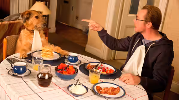 Neil (Simon Pegg) pointing at his dog during breakfast