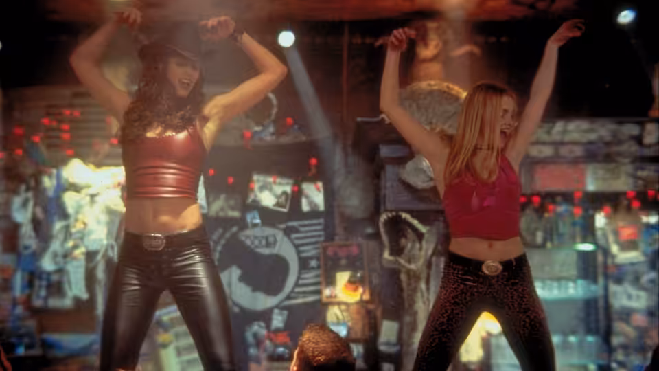 Two women dance on a bar counter with arms raised high