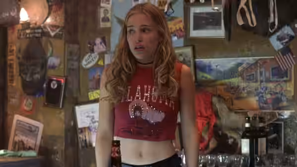 Woman in red Oklahoma crop top stands in a poster-filled room