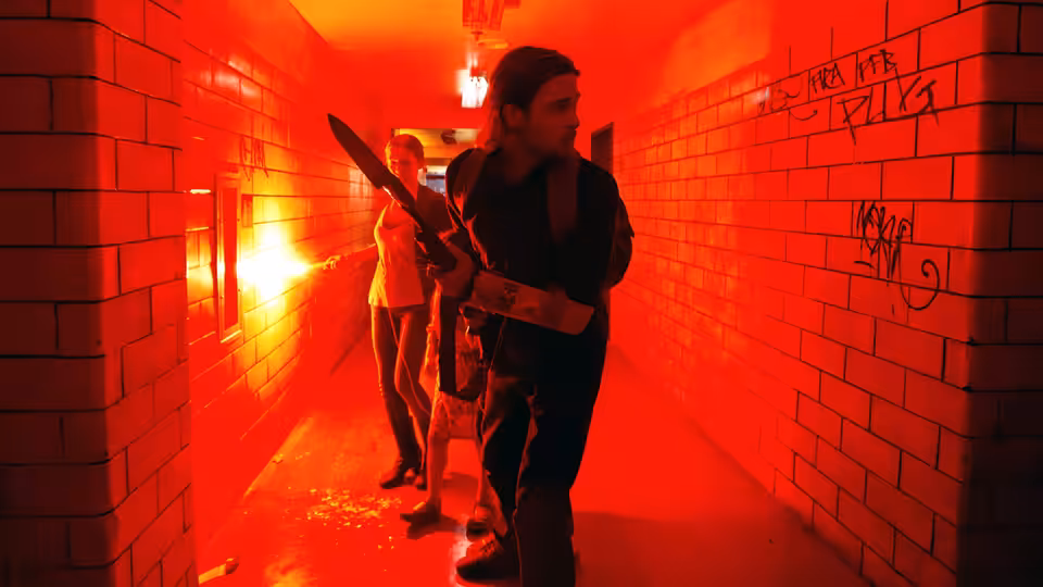 A man carrying a rifle leads a woman through a red-lit corridor