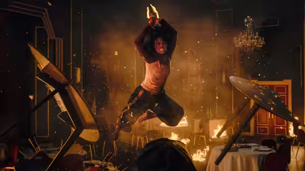 A woman raises a knife overhead amid overturned furniture and flames