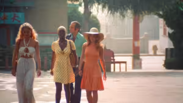 Three women and a man walk together along a sunlit street