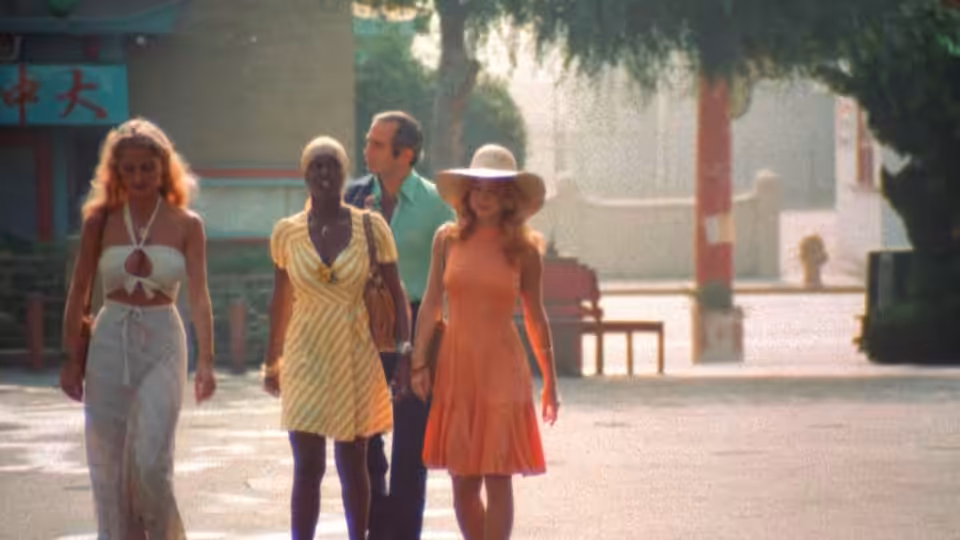 Three women and a man walk together along a sunlit street