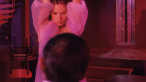 A woman in a sheer white outfit raises her arms inside a dim club