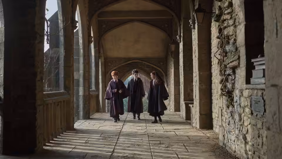 Three students in Hogwarts robes walk through a stone archway