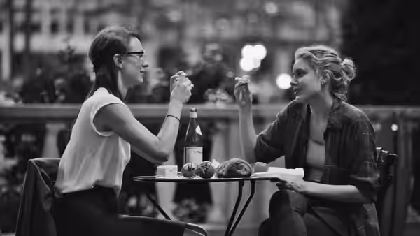 Frances (Greta Gerwig) and Sophie (Mickey Sumner) toasting at an outdoor table