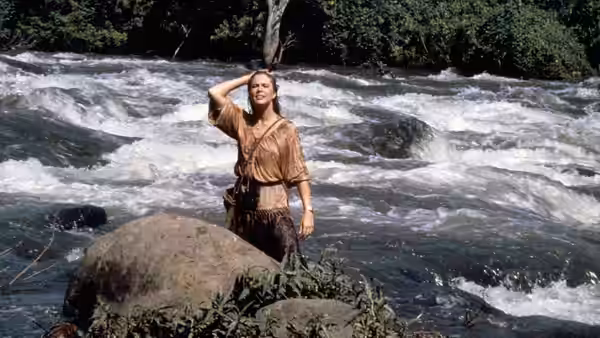 Joan Wilder (Kathleen Turner) stands beside a rushing river