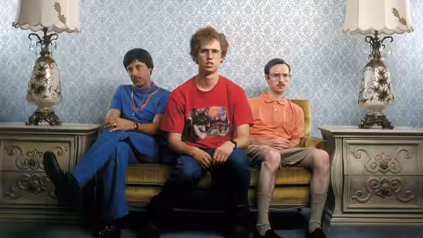 Napoleon Dynamite (Jon Heder) sits between Kip and Uncle Rico on a couch